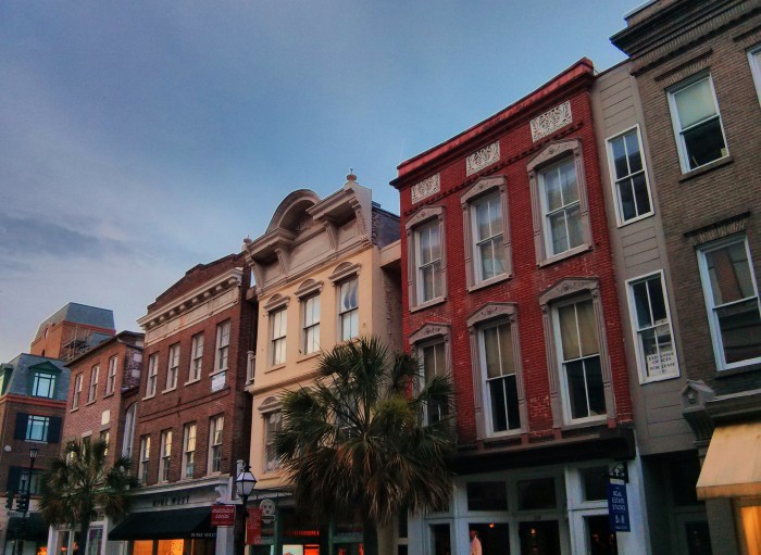 The lights in the stores on King Street in Charleston, SC, come on as the setting sun illuminates the buildings.