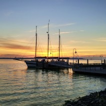 The sun rising over Charleston Harbor is captured through the rigging of the three-masted schooner Pride.