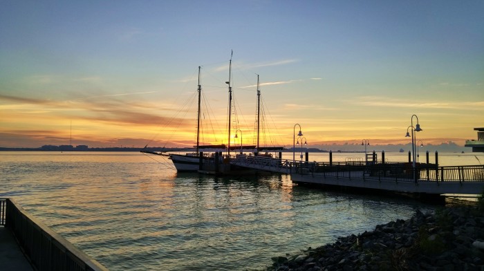 The sun rising over Charleston Harbor is captured through the rigging of the three-masted schooner Pride.